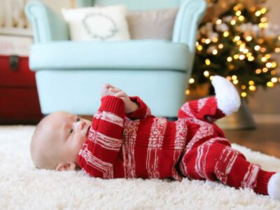 baby in Christmas pajamas playing with hand